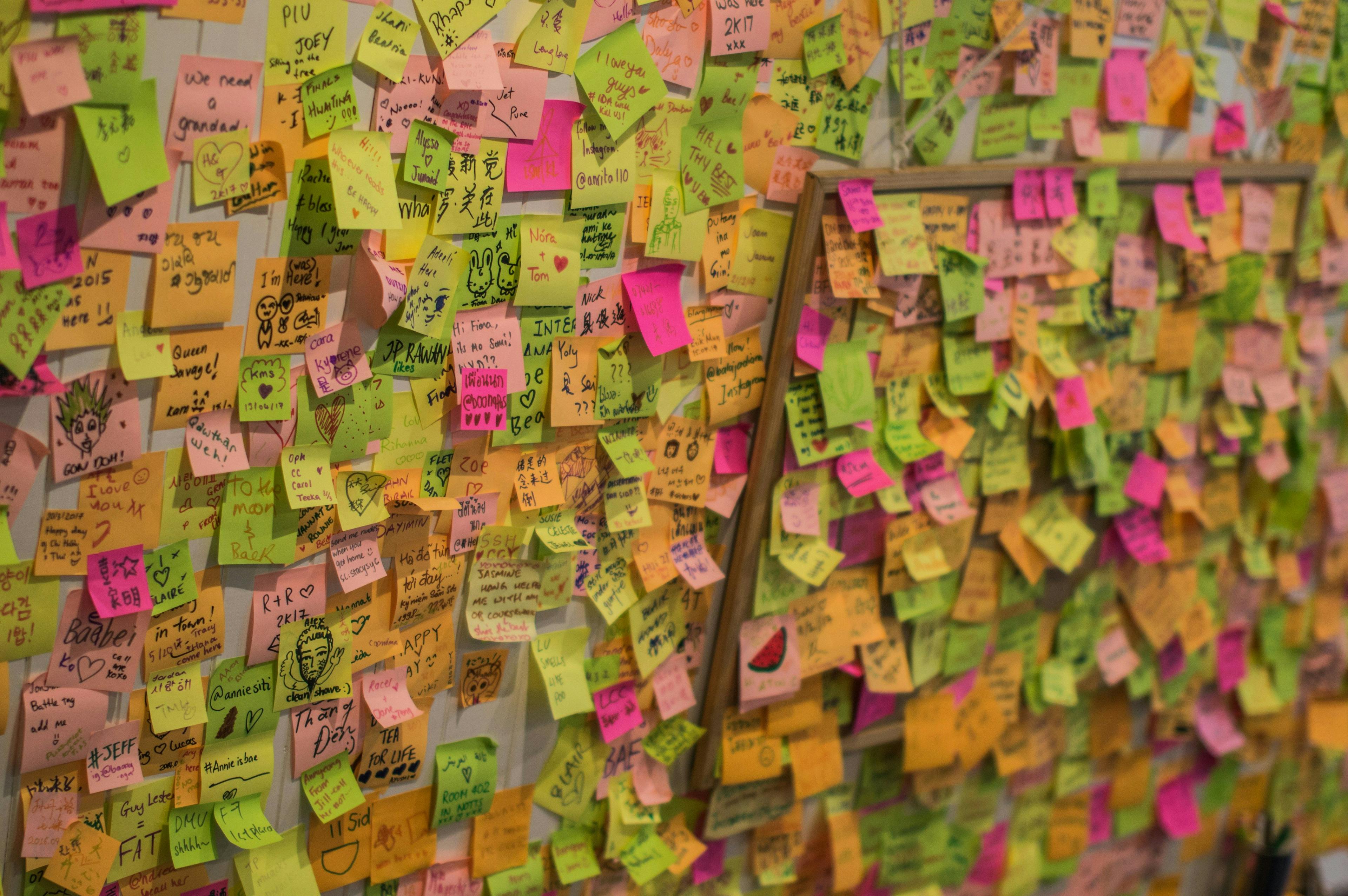 A bulletin board covered in post-it notes, symbolizing brainstorming and idea generation, in a bright, indoor setting, Photographic, using a wide-angle lens to capture the expanse of the bulletin board.