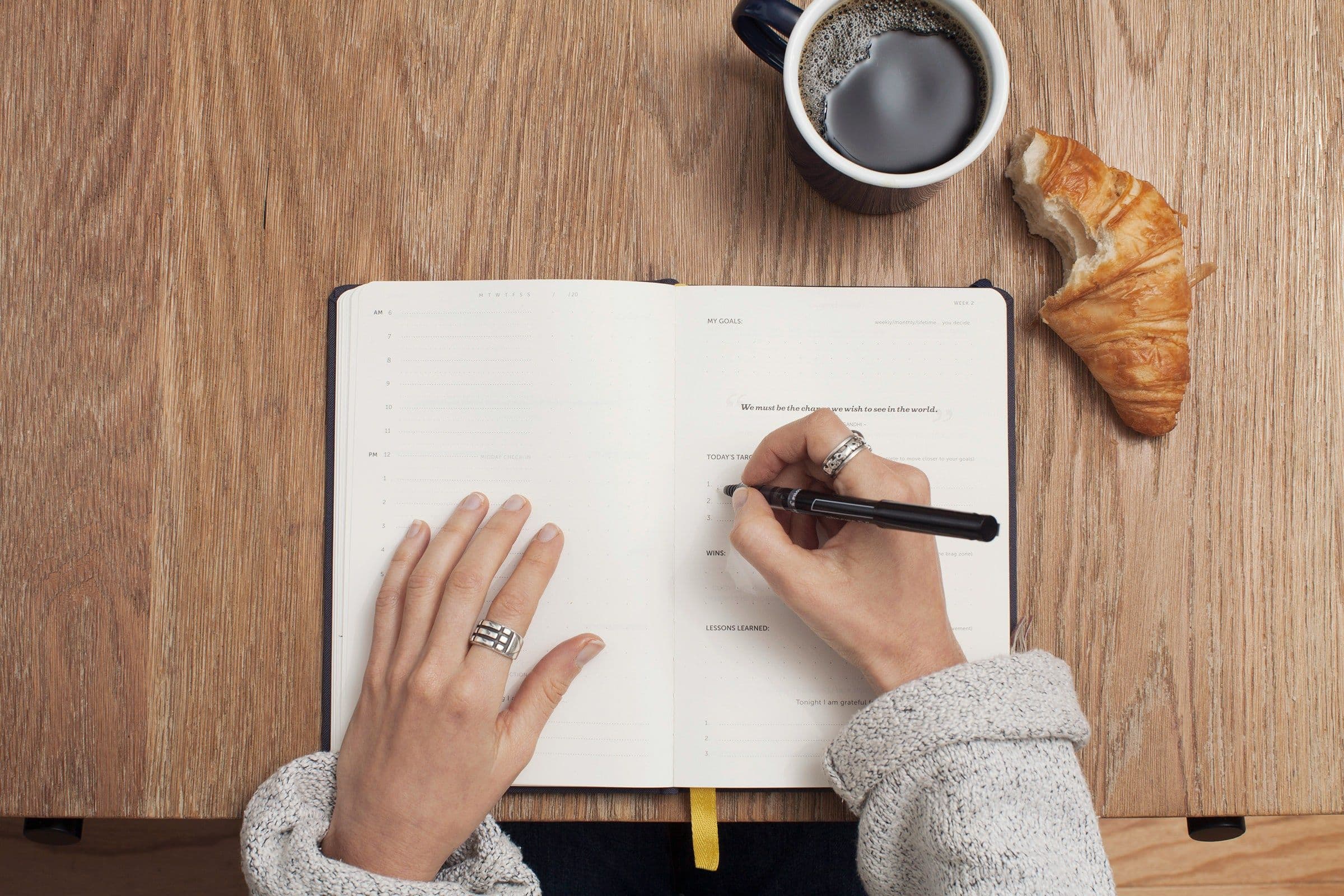 la mano de una mujer escribiendo en un cuaderno con una taza de café